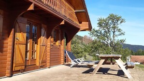 Una cabaña de madera con un balcón, un patio con mesa y sillas, y vistas del paisaje circundante.