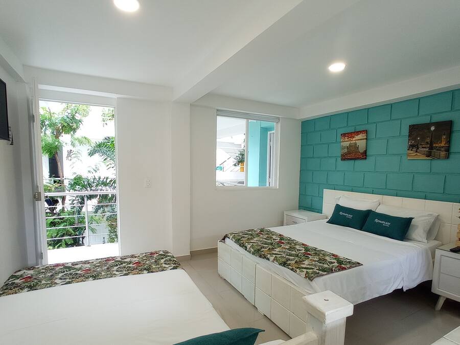 Un dormitorio con dos camas, una pared de acento color turquesa y un balcón con vistas a la vegetación.
