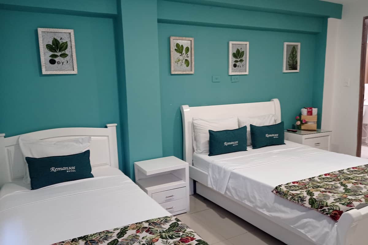 A hotel room with two beds, teal walls, and framed botanical prints.