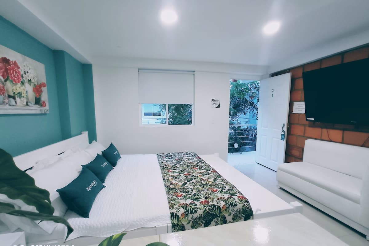 A modern bedroom with a bed, a white sofa, a TV, and a window with a view of the outside.