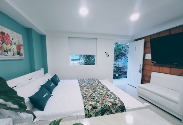 A modern bedroom with a bed, a white sofa, a TV, and a window with a view of the outside. - Hotel Boutique Los Remansos (Palmira)