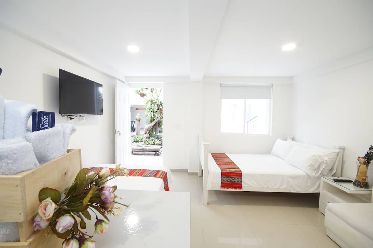 A modern hotel room with a bed, a TV, a small table with a vase, and a window.