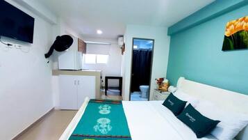 A hotel room with a bed, a TV mounted on the wall, a kitchen area, and a bathroom visible through an open door.