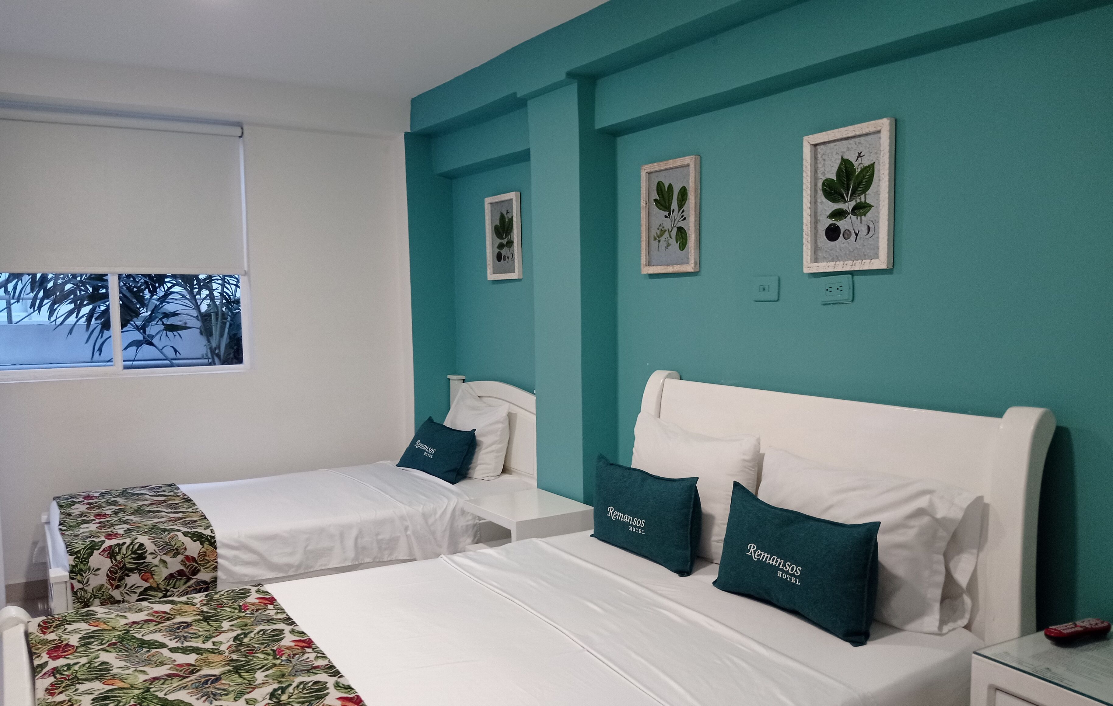A hotel room with two beds, teal walls, and framed botanical prints.