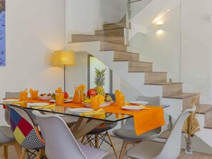 A modern dining area with a glass table, orange tablecloth, and a variety of fruits and beverages.