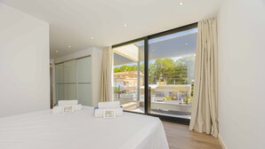 A hotel room with a large bed, a sliding glass door to a balcony, and a view of buildings and trees outside. - Villa Jade II (Can Picafort)