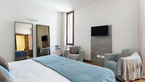 A hotel room with a bed, two armchairs, a TV, and a window.