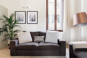 En stue med en mørkebrun sofa, en stor grøn plante og to billeder i rammer på væggen.