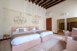 Quarto de hotel com duas camas, um lustre, um espelho grande e teto de madeira.