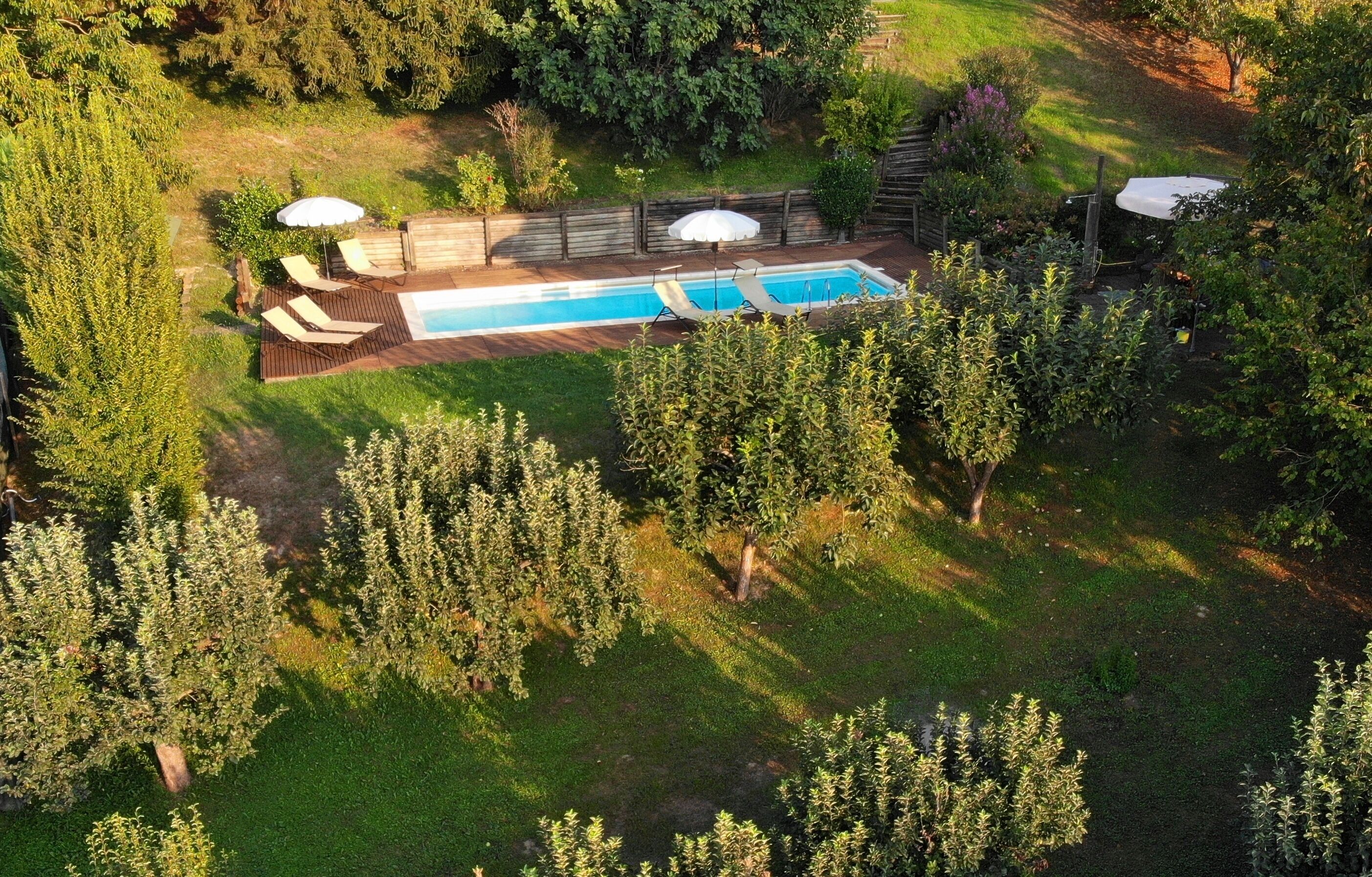 An aerial view of a backyard with a swimming pool, wooden deck, and lounge chairs.