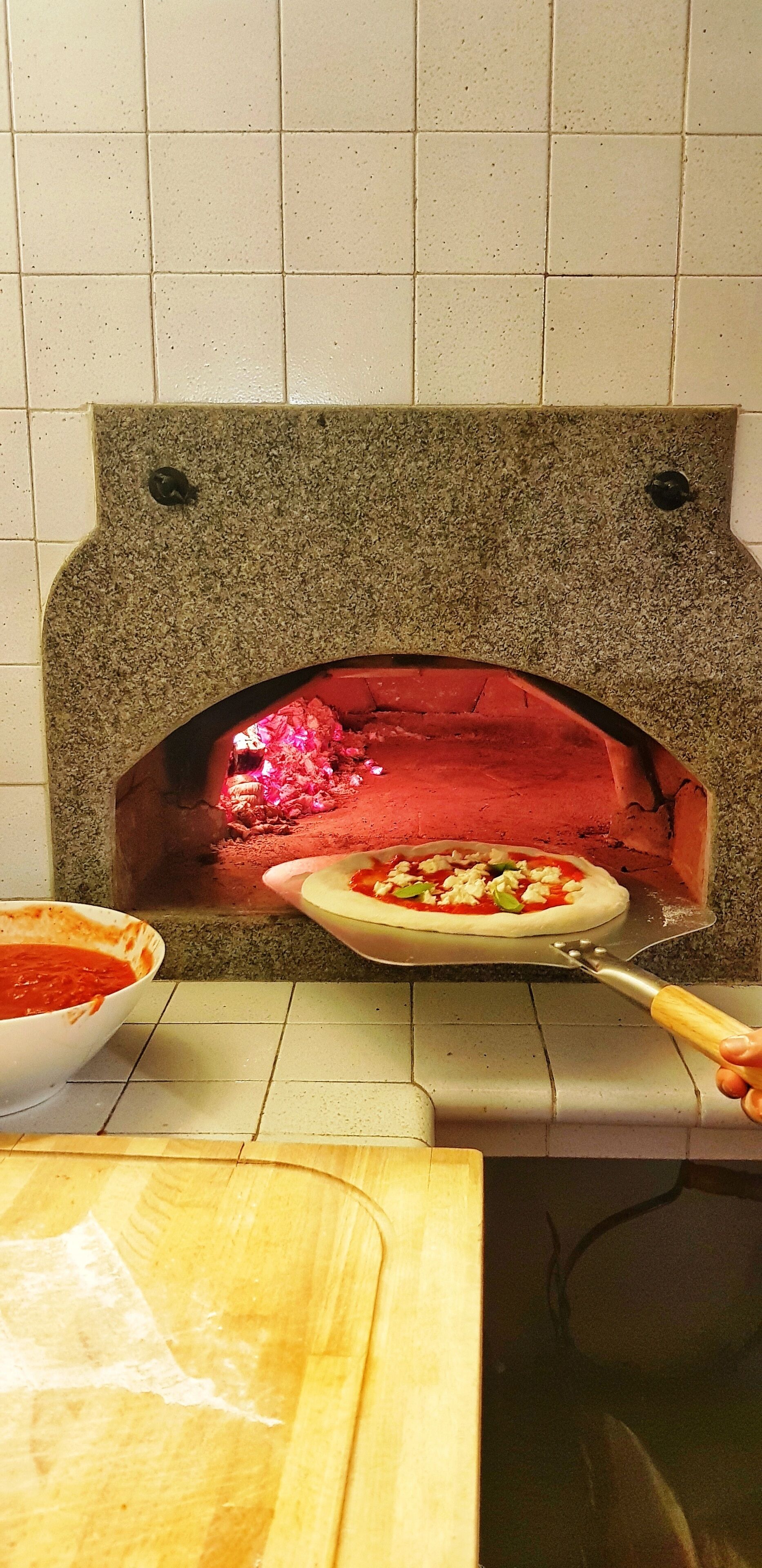 En stenovn med pizza indeni, en pizzaskærer og en skål med sauce på en bordplade.