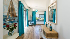 A room with a wooden floor, a dining table with chairs, a blue armchair, and a large window with a view of the sea. - Premium Beachfront Villa With Private Pool & Panoramic Sea Views From Any Angle (Rethymno)
