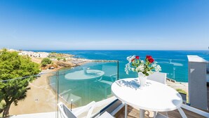 A balcony with a clear view of the sea, a white table with a vase of flowers, and a sandy beach area. - Premium Beachfront Villa With Private Pool & Panoramic Sea Views From Any Angle (Rethymno)