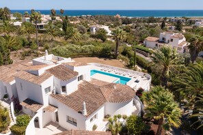 Une villa blanche avec une piscine, entourée de palmiers et offrant une vue sur la mer.