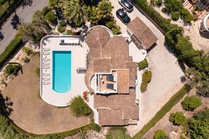 An aerial view of a property with a swimming pool, a covered patio, and a landscaped garden.