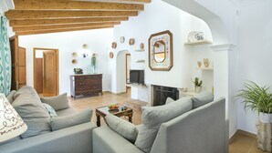 Een woonkamer met een bank, salontafel en open haard. Er staan decoratieve items op de muren en er is een televisie.
