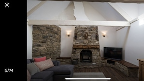 Una sala de estar acogedora con chimenea de piedra, un televisor de pantalla plana y un sofá de color oscuro.