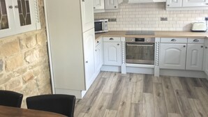 Una cocina moderna con armarios blancos, horno empotrado, microondas y una pared de piedra.