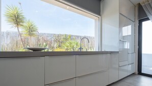 A modern kitchen with white cabinets and a large window overlooking a garden. - Modern accessible villa [17] (Luz)