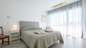 A modern hotel room with a large bed, bedside tables, a chair, and a view of the outdoors through sheer curtains. - Modern accessible villa [17] (Luz)