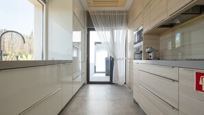 A modern kitchen with light wood cabinets, a stainless steel range hood, and a view through a doorway to a balcony. - Modern accessible villa [17] (Luz)