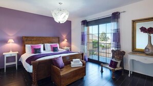 A bedroom with a wooden bed, two bedside lamps, a nightstand, a bench with towels, a chair, a window with curtains, and a vase with flowers on a table. - Luxury Villa near to Mijas Pueblo that sleeps 14. With Large Private Heated Pool (Mijas)