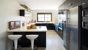 A modern kitchen with a central island, two bar stools, a large refrigerator, and a window providing natural light. - Luxury Villa near to Mijas Pueblo that sleeps 14. With Large Private Heated Pool (Mijas)