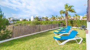 A poolside area with blue and white lounge chairs, palm trees, and a view of buildings in the background. - MARINA D'OR IV CASA 5 - Chalet with shared pool in Cala D'Or. Free WiFi (Santanyí)