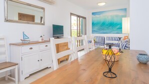 A dining area with a wooden table, white chairs, a TV, and a painting of a wave. - MARINA D'OR IV CASA 5 - Chalet with shared pool in Cala D'Or. Free WiFi (Santanyí)