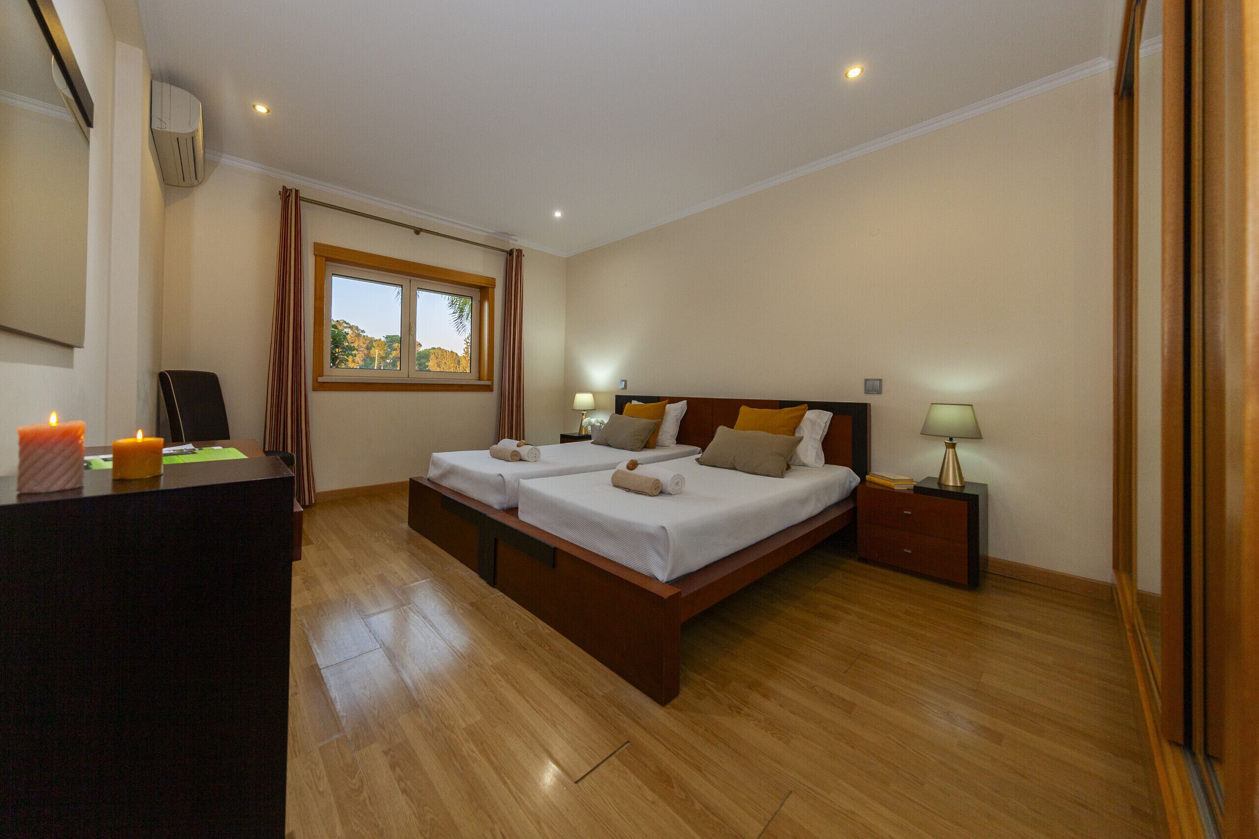 Una habitació d'hotel amb dos llits, un escriptori, una finestra amb cortines i una nit falda amb una làmpada.