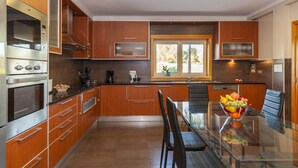 Una cucina moderna con mobili in legno, elettrodomestici in acciaio inossidabile e un tavolo da pranzo in vetro con una ciotola di frutta.