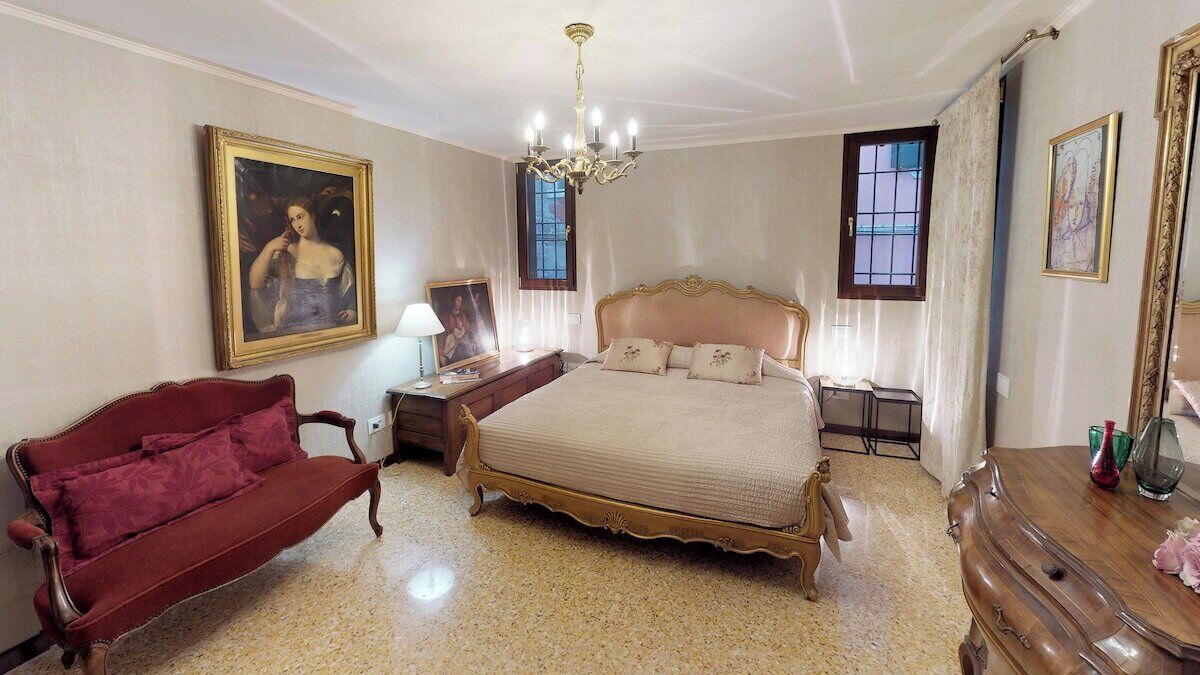 Un dormitorio con una cama grande, un sofá rojo, una araña y un cuadro en la pared.