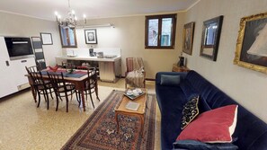 A living room with a blue sofa, a dining table with chairs, a kitchen area, and a patterned rug. - Ca' Moro - Murano (Venice)