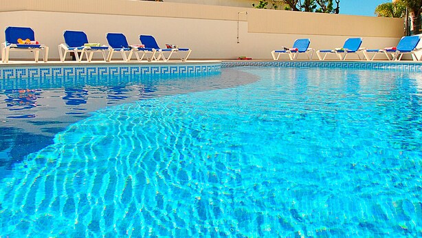 A clear swimming pool with blue water, surrounded by lounge chairs.