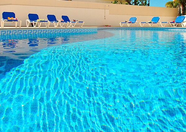 A clear swimming pool with blue water, surrounded by lounge chairs.