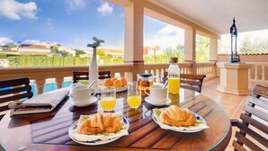A breakfast table with croissants, orange juice, and coffee on a balcony with a view of a pool and buildings. - Beautiful villa with private pool excelent for families. Aircond and wifi available - Free Wifi (Llucmajor)