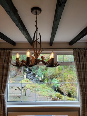 Enjoy a serene view of the lush garden with a waterfall from the comfort of this room, featuring a rustic ceiling and modern lighting.