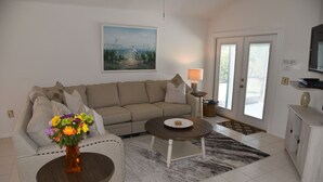 Un soggiorno con un divano color beige, un tavolino da caffè, un vaso con fiori, un quadro appeso al muro e un televisore su un mobile.