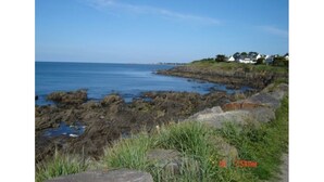 A coastal landscape with rocky terrain and a clear view of the sea. There are houses on a grassy hill in the background. - 3 Bedroom mobile home Brittany 580 (Pont-Aven)