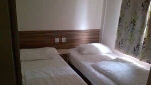 A small, simple room with two single beds, wooden headboards, and a window with floral curtains. - 3 Bedroom mobile home Brittany 580 (Pont-Aven)