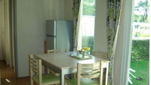 A dining area with a table and chairs, a refrigerator, and a view of a garden through the window. - 3 Bedroom mobile home Brittany 580 (Pont-Aven)