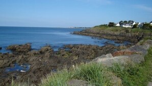 A coastal landscape with rocky terrain and a clear view of the sea. There are houses on a grassy hill in the background. - 3 Bedroom mobile home Brittany 580 (Pont-Aven)