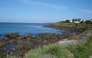 A coastal landscape with rocky terrain and a clear view of the sea. There are houses on a grassy hill in the background. - 3 Bedroom mobile home Brittany 580 (Pont-Aven)