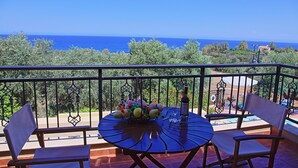 Un balcon avec une table dressée pour deux personnes, offrant une vue panoramique sur la mer et la verdure.