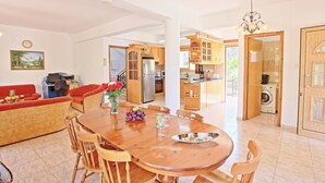 Un vaste espace de vie comprenant une table à manger en bois, des canapés rouges et une cuisine à l’arrière-plan.