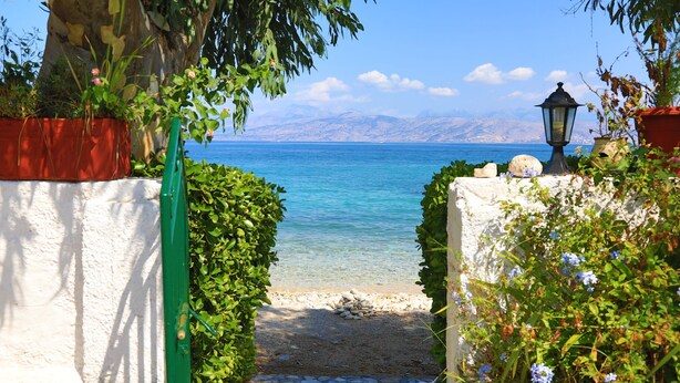Un sentier de pierres mène à une plage d’où l’on a une vue dégagée sur la mer et les montagnes au loin.