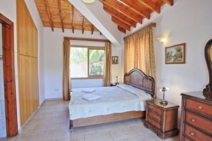 Una camera da letto con soffitto in legno, un letto con copripiumino bianco, un comodino con lampada e una cassettiera.