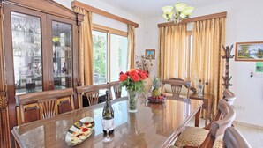 Un coin repas avec une table en bois, des chaises, un lustre et une fenêtre avec des rideaux.