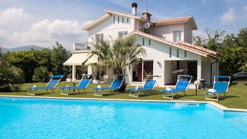 Une grande maison avec une piscine, des fauteuils de jardin bleus et un jardin.