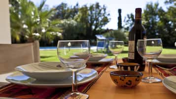 Un tavolo apparecchiato all'aperto, con piatti, ciotole e bicchieri da vino, una bottiglia di vino e vista su un giardino con palme.
